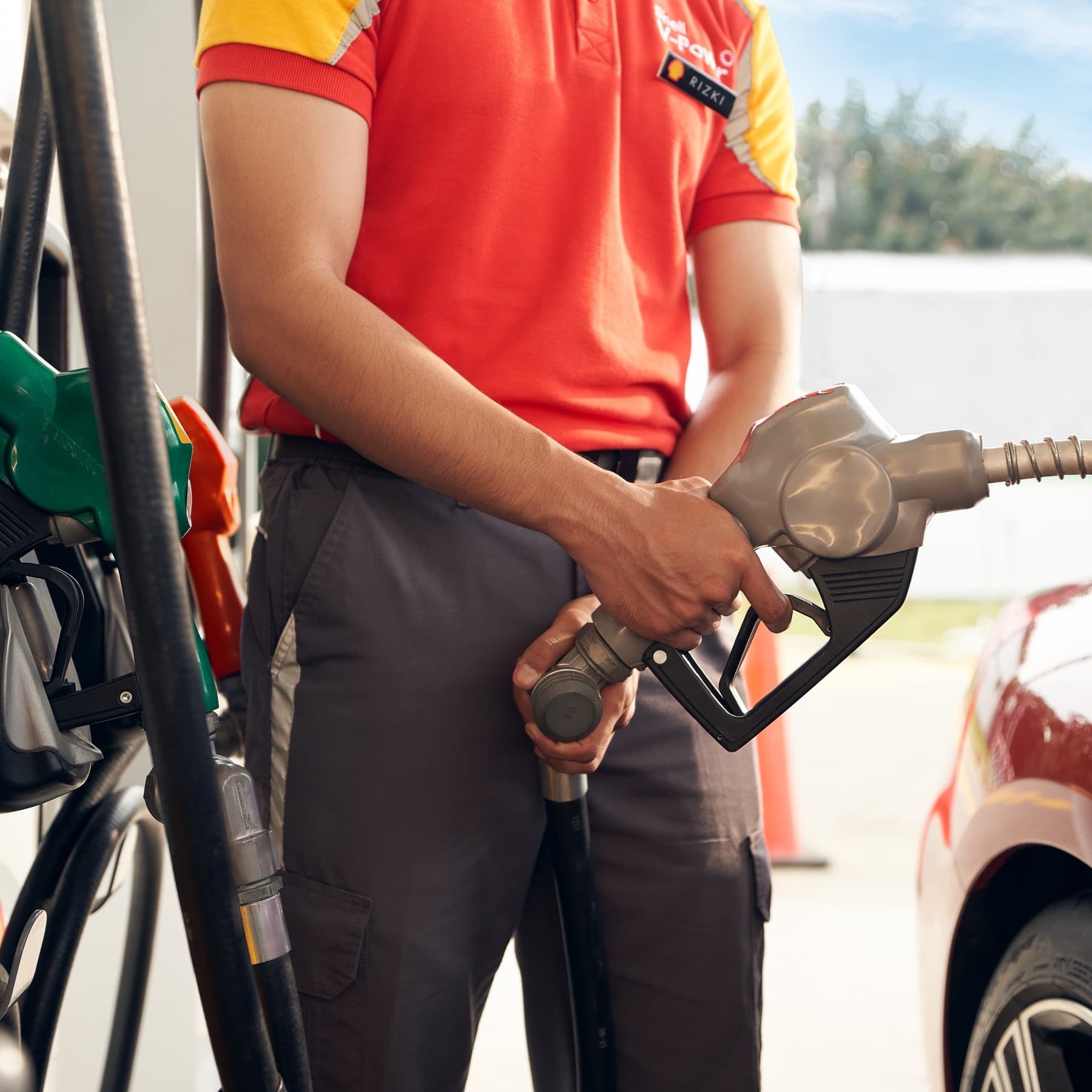 Attendant in a red Shell uniform holding a fuel nozzle at a pump